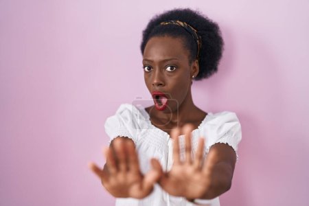 Téléchargez les photos : African woman with curly hair standing over pink background moving away hands palms showing refusal and denial with afraid and disgusting expression. stop and forbidden. - en image libre de droit