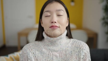 Téléchargez les photos : Jeune femme chinoise assise sur un canapé respirant à la maison - en image libre de droit