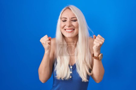 Téléchargez les photos : Femme blanche debout sur fond bleu excité pour le succès avec les bras levés et les yeux fermés célébrant la victoire en souriant. concept gagnant. - en image libre de droit