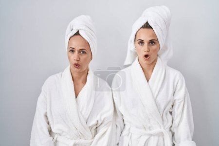 Téléchargez les photos : Femme et fille d'âge moyen portant un peignoir blanc et une serviette effrayées et choquées par l'expression surprise, la peur et le visage excité. - en image libre de droit
