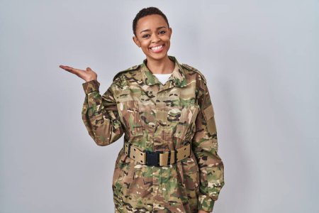 Photo for Beautiful african american woman wearing camouflage army uniform smiling cheerful presenting and pointing with palm of hand looking at the camera. - Royalty Free Image