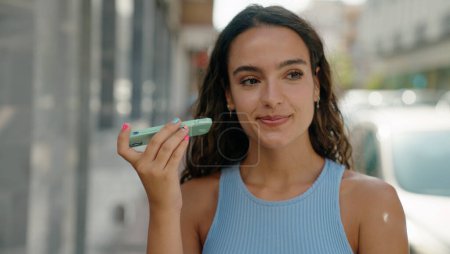 Foto de Joven hermosa mujer hispana sonriendo confiado escuchando mensaje de audio por el teléfono inteligente en la calle - Imagen libre de derechos