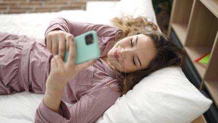 Téléchargez les photos : Jeune belle femme hispanique utilisant smartphone couché sur le lit dans la chambre - en image libre de droit