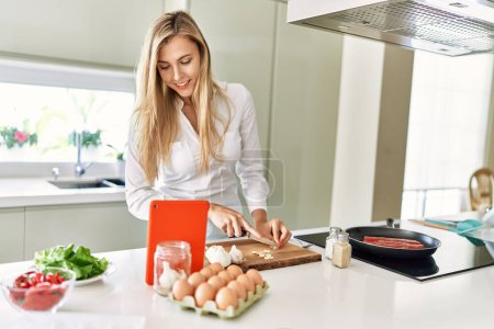 Téléchargez les photos : Jeune femme blonde utilisant la cuisine touchpad à la cuisine - en image libre de droit