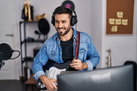 Foto de Joven hispano sonriendo confiado sosteniendo la guitarra eléctrica en el estudio de música - Imagen libre de derechos