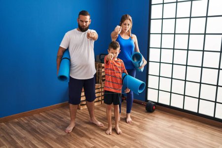 Foto de Family of three holding yoga mat pointing with finger to the camera and to you, confident gesture looking serious - Imagen libre de derechos