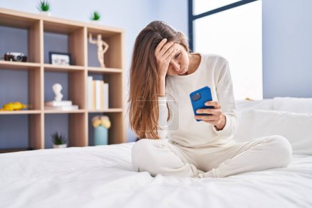 Photo for Young woman using smartphone with worried expression at bedroom - Royalty Free Image