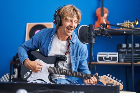 Téléchargez les photos : Young man artist singing song playing electrical guitar at music studio - en image libre de droit