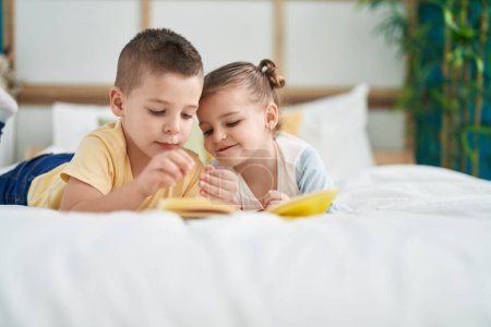 Foto de Two kids reading story book lying on bed at bedroom - Imagen libre de derechos