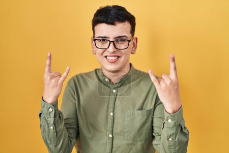 Photo for Non binary person standing over yellow background shouting with crazy expression doing rock symbol with hands up. music star. heavy concept. - Royalty Free Image