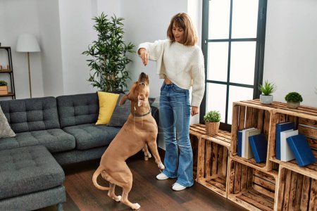Foto de Joven caucásico mujer alimentación perro de pie en casa - Imagen libre de derechos