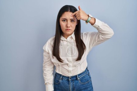 Téléchargez les photos : Young latin woman standing over blue background pointing unhappy to pimple on forehead, ugly infection of blackhead. acne and skin problem - en image libre de droit