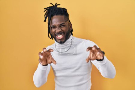 Photo for African man with dreadlocks wearing turtleneck sweater over yellow background smiling funny doing claw gesture as cat, aggressive and sexy expression - Royalty Free Image