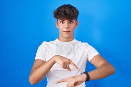 Photo for Hispanic teenager standing over blue background in hurry pointing to watch time, impatience, upset and angry for deadline delay - Royalty Free Image