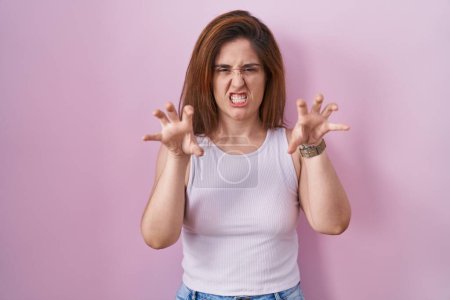 Téléchargez les photos : Femme brune debout sur fond rose souriant drôle faisant griffe geste comme chat, expression agressive et sexy - en image libre de droit