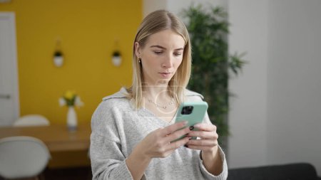 Foto de Mujer rubia joven usando el teléfono inteligente en casa - Imagen libre de derechos