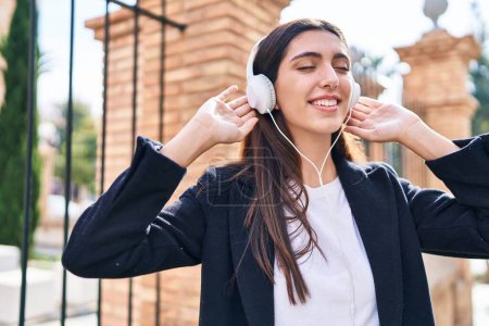 Foto de Joven mujer hispana hermosa escuchando música de pie en la calle - Imagen libre de derechos