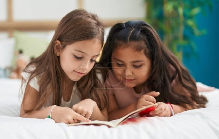 Foto de Dos niños leyendo el libro acostados en la cama en el dormitorio - Imagen libre de derechos