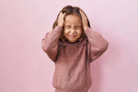 Photo for Little hispanic girl standing over pink background suffering from headache desperate and stressed because pain and migraine. hands on head. - Royalty Free Image