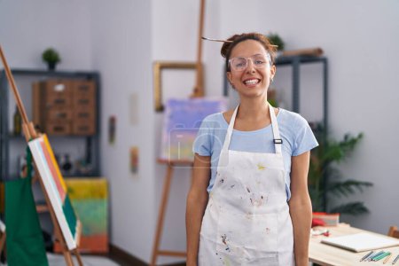 Photo for Brunette woman painting at art studio looking positive and happy standing and smiling with a confident smile showing teeth - Royalty Free Image