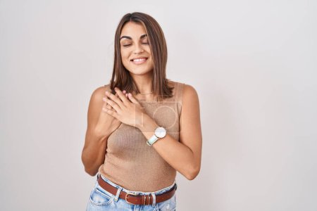 Téléchargez les photos : Young hispanic woman standing over white background smiling with hands on chest with closed eyes and grateful gesture on face. health concept. - en image libre de droit