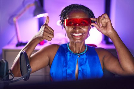 Téléchargez les photos : Femme africaine avec dreadlocks jouer à des jeux vidéo portant des lunettes de réalité virtuelle souriant heureux et positif, pouce levé faire excellent et signe d'approbation - en image libre de droit