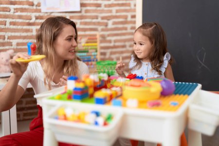 Photo for Teacher and toddler playing with construction blocks sitting on table at kindergarten - Royalty Free Image