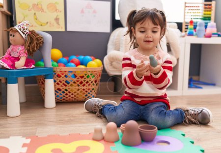 Foto de Adorable hispanic girl playing with toys sitting on floor at kindergarten - Imagen libre de derechos