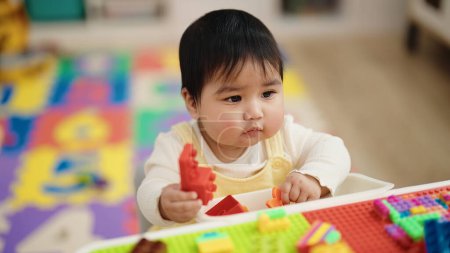 Photo for Adorable hispanic baby playing with construction blocks sitting on table at kindergarten - Royalty Free Image