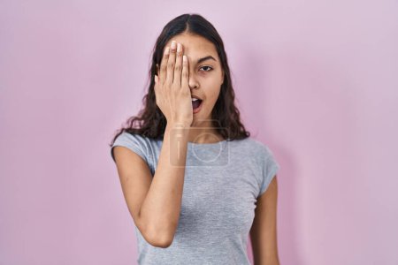 Photo for Young brazilian woman wearing casual t shirt over pink background covering one eye with hand, confident smile on face and surprise emotion. - Royalty Free Image