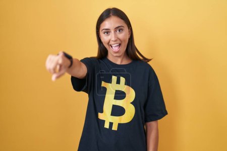Téléchargez les photos : Jeune femme hispanique portant Bitcoin t-shirt pointant vers vous et la caméra avec les doigts, souriant positif et joyeux - en image libre de droit