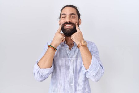 Foto de Hombre hispano con barba vistiendo camisa casual sonriendo con la boca abierta, los dedos señalando y forzando una sonrisa alegre - Imagen libre de derechos