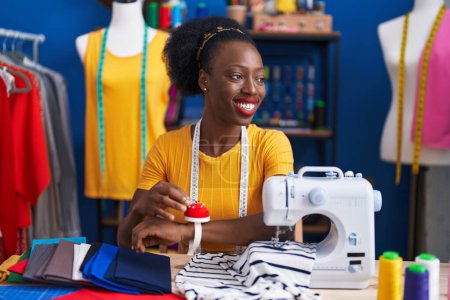Téléchargez les photos : African american woman tailor using sewing machine holding pin at sewing studio - en image libre de droit