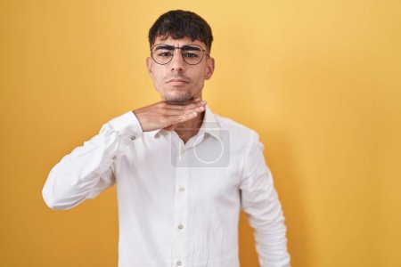 Téléchargez les photos : Jeune homme hispanique debout sur fond jaune couper la gorge avec la main comme couteau, menacer d'agression avec une violence furieuse - en image libre de droit