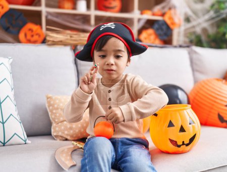 Photo for Adorable hispanic boy having halloween party holding pumpkin basket and candy at home - Royalty Free Image
