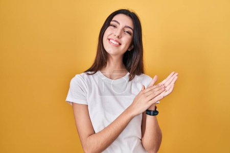 Téléchargez les photos : Young beautiful woman standing over yellow background clapping and applauding happy and joyful, smiling proud hands together - en image libre de droit