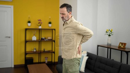 Téléchargez les photos : Homme d'âge moyen souffrant de maux de dos debout à la maison - en image libre de droit