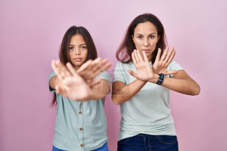 Téléchargez les photos : Young mother and daughter standing over pink background rejection expression crossing arms and palms doing negative sign, angry face - en image libre de droit