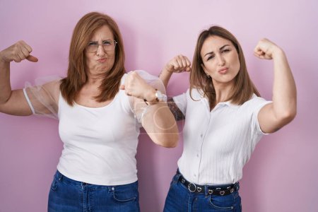 Téléchargez les photos : Hispanic mother and daughter wearing casual white t shirt over pink background showing arms muscles smiling proud. fitness concept. - en image libre de droit