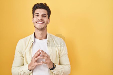 Photo for Young hispanic man standing over yellow background hands together and fingers crossed smiling relaxed and cheerful. success and optimistic - Royalty Free Image