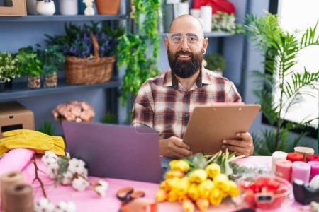 Téléchargez les photos : Jeune homme chauve fleuriste en utilisant un document de lecture d'ordinateur portable à la boutique de fleurs - en image libre de droit