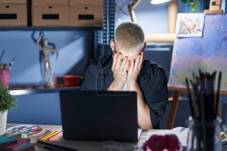Photo for Young caucasian man using laptop at night at art studio with sad expression covering face with hands while crying. depression concept. - Royalty Free Image