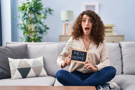 Photo for Hispanic woman with curly hair sitting on the sofa at new home afraid and shocked with surprise and amazed expression, fear and excited face. - Royalty Free Image