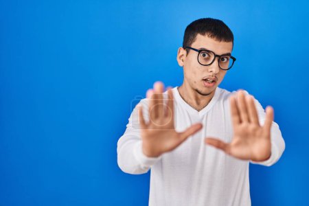 Photo for Young arab man wearing casual white shirt and glasses afraid and terrified with fear expression stop gesture with hands, shouting in shock. panic concept. - Royalty Free Image