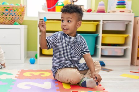 Photo for African american boy holding wooden piece sitting on floor at kindergarten - Royalty Free Image