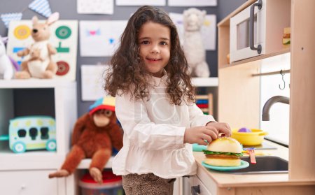 Téléchargez les photos : Adorable fille hispanique jouant pour cuisiner jouet hamburger avec cuisine de jeu à la maternelle - en image libre de droit