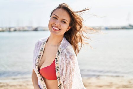 Foto de Joven mujer hispana hermosa turista sonriendo confiada vistiendo bikini en la playa - Imagen libre de derechos