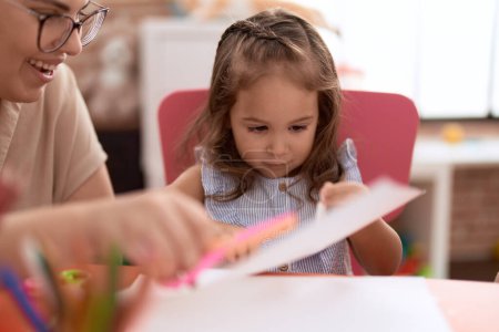 Téléchargez les photos : Teacher and toddler smiling confident cutting paper at kindergarten - en image libre de droit