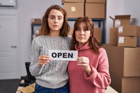 Téléchargez les photos : Two women working at small business ecommerce holding open banner relaxed with serious expression on face. simple and natural looking at the camera. - en image libre de droit