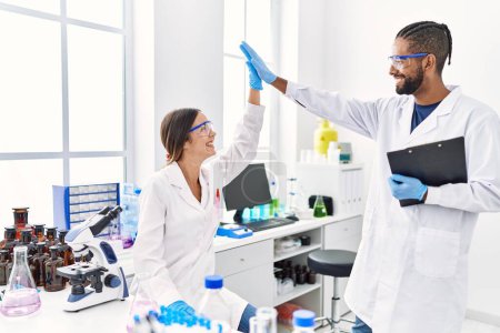 Photo for Man and woman scientist partners holding clipboard high five raised up hands at laboratory - Royalty Free Image